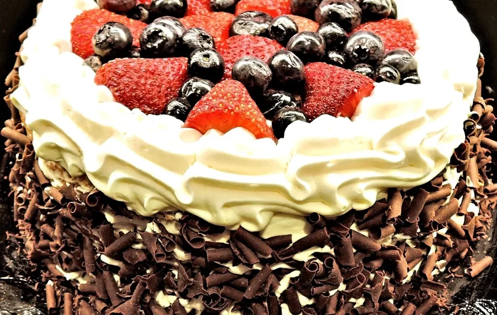 Cake topped with whipped cream, berries and chocolate shavings