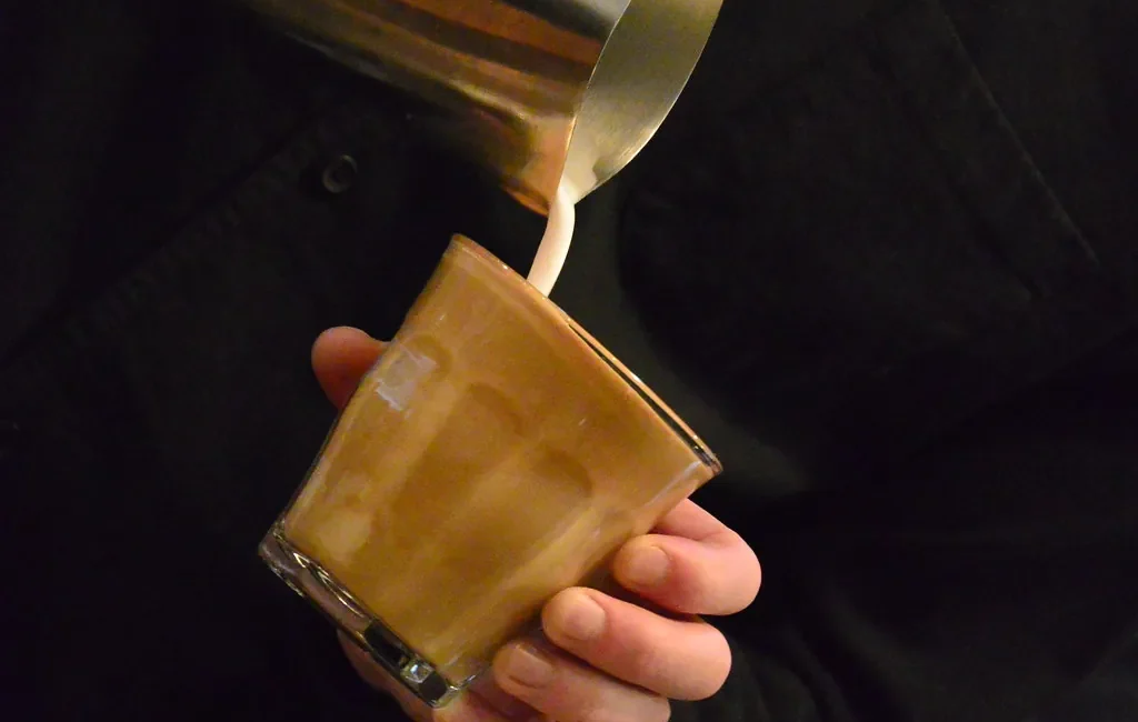Milk being poured into a glass of coffee
